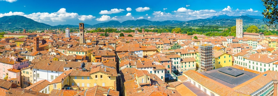 Aerial top panoramic view of historical centre medieval town Lucca with old buildings, typical orange terracotta tiled roofs and mountain range, hills, blue sky white clouds background, Tuscany, Italy