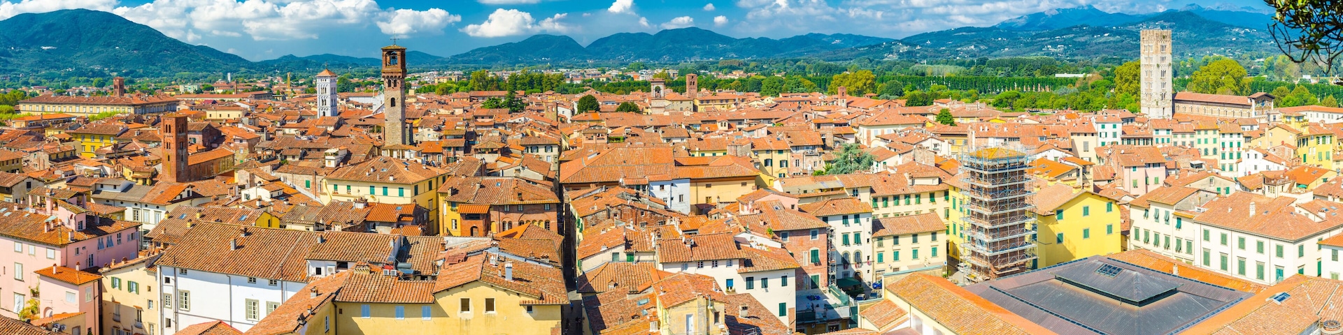 Aerial top panoramic view of historical centre medieval town Lucca with old buildings, typical orange terracotta tiled roofs and mountain range, hills, blue sky white clouds background, Tuscany, Italy