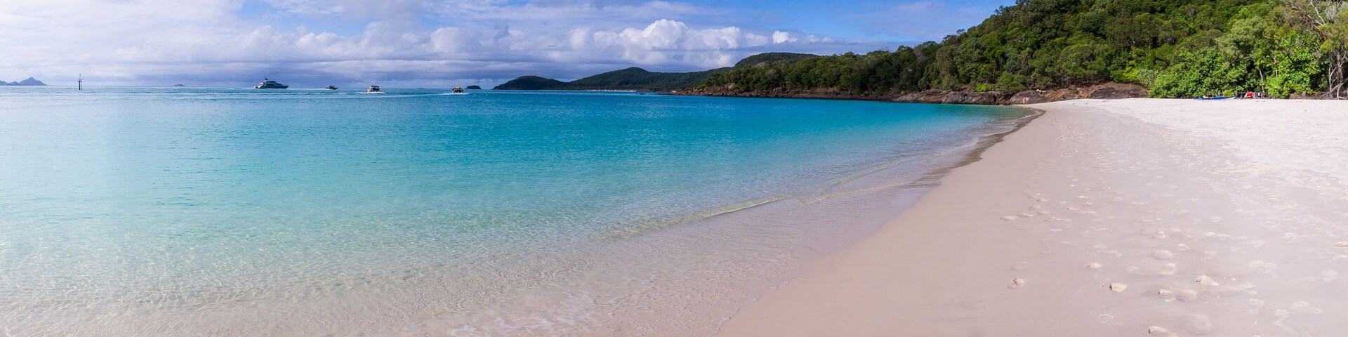 Uma praia com águas turquesa cristalinas, areia branca e um morro coberto por vegetação.