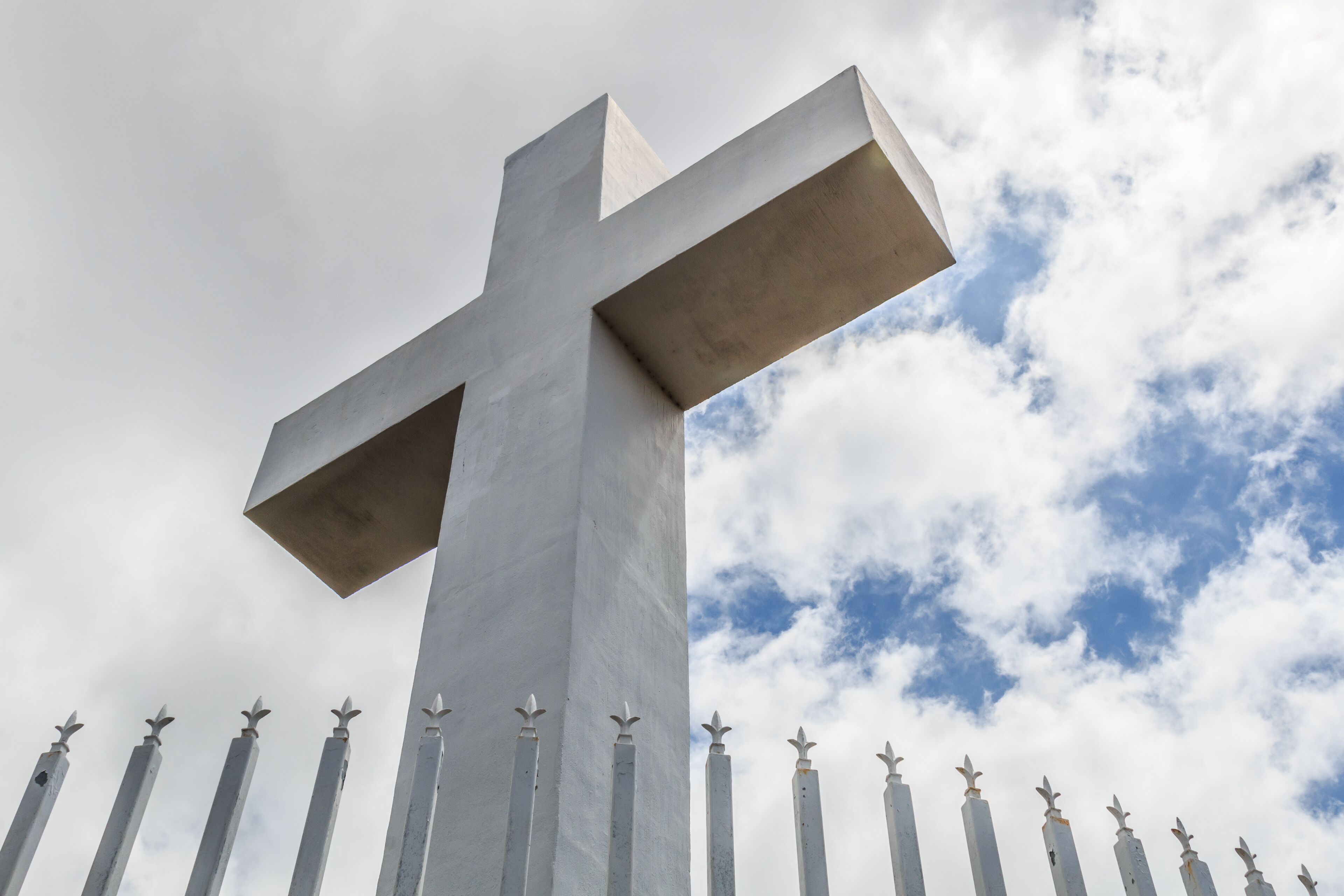 Mt. Helix cross with fence railing and a background of a cloudy blue sky in La Mesa, a city in San Diego, California.  