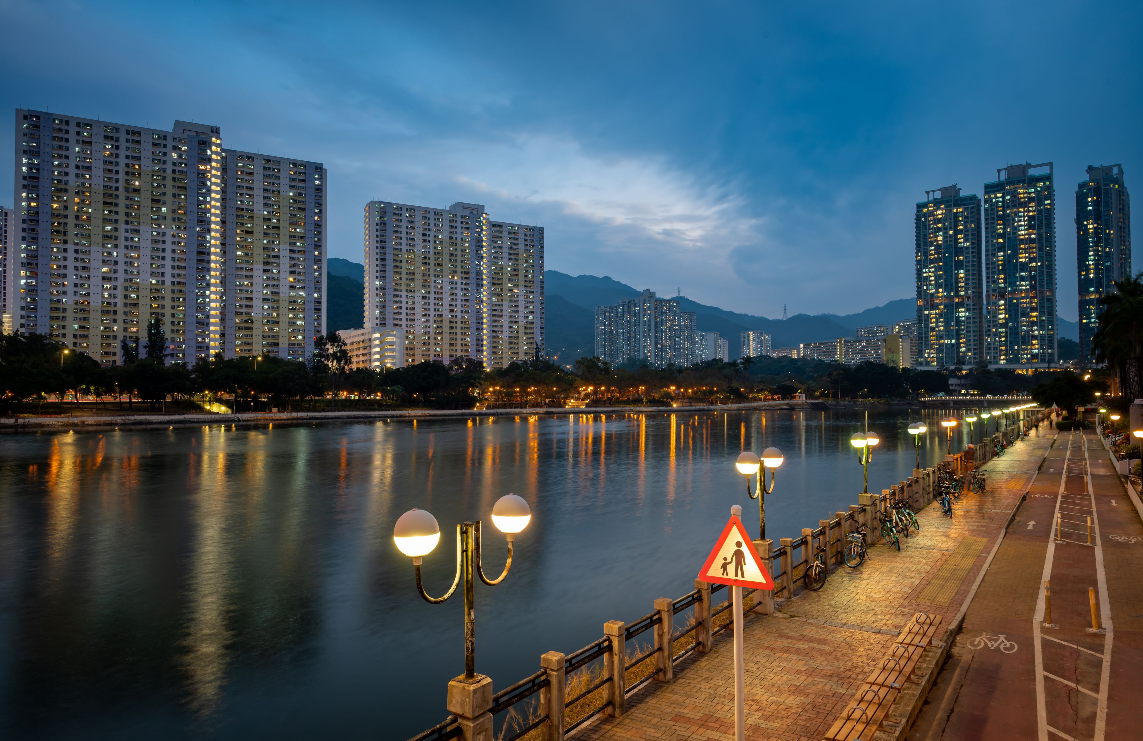 A river with a cityscape in the background, including high-rise buildings and a mountain range.