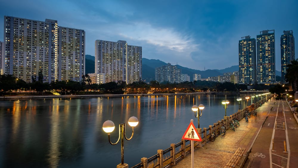A river with a cityscape in the background, including high-rise buildings and a mountain range.