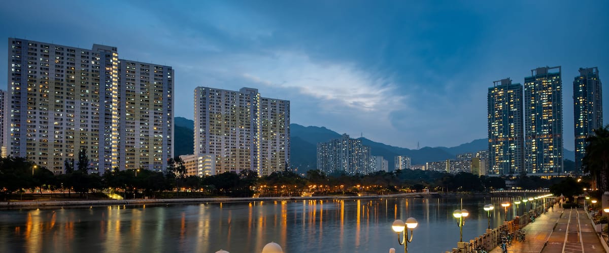 Um rio com um horizonte urbano ao fundo, incluindo edifícios altos e uma cordilheira.