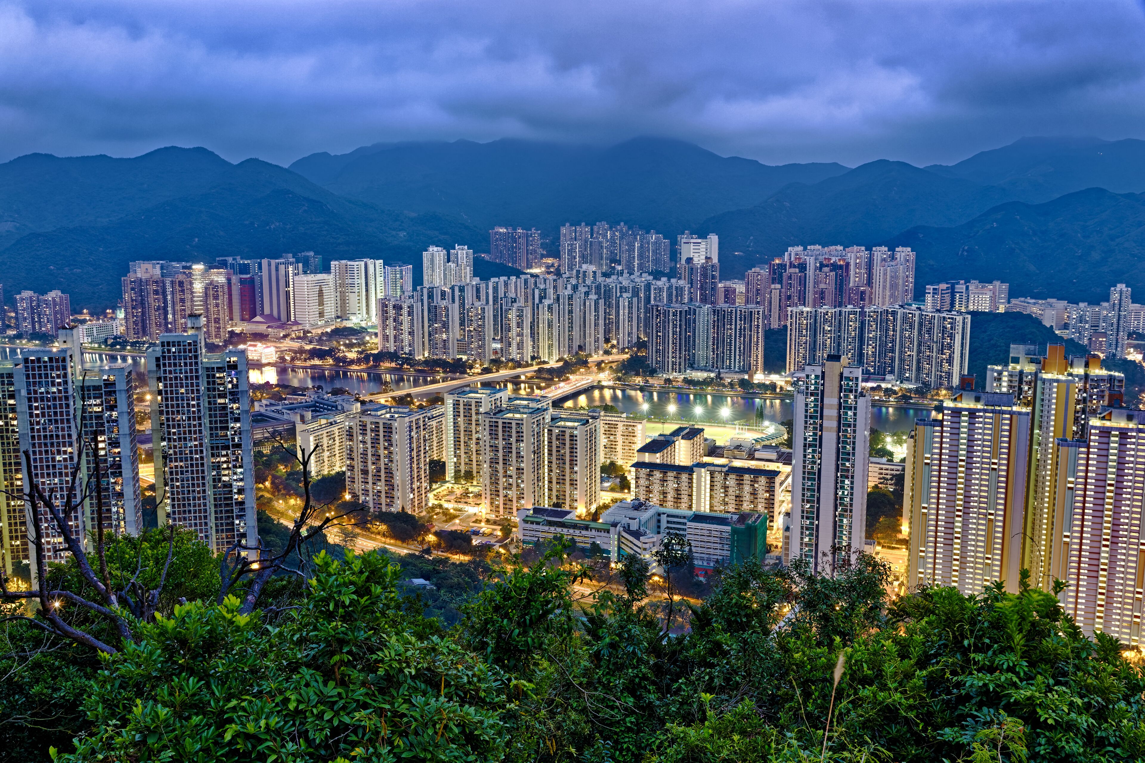 A cityscape with high-rise buildings, a river, and mountains in the background.