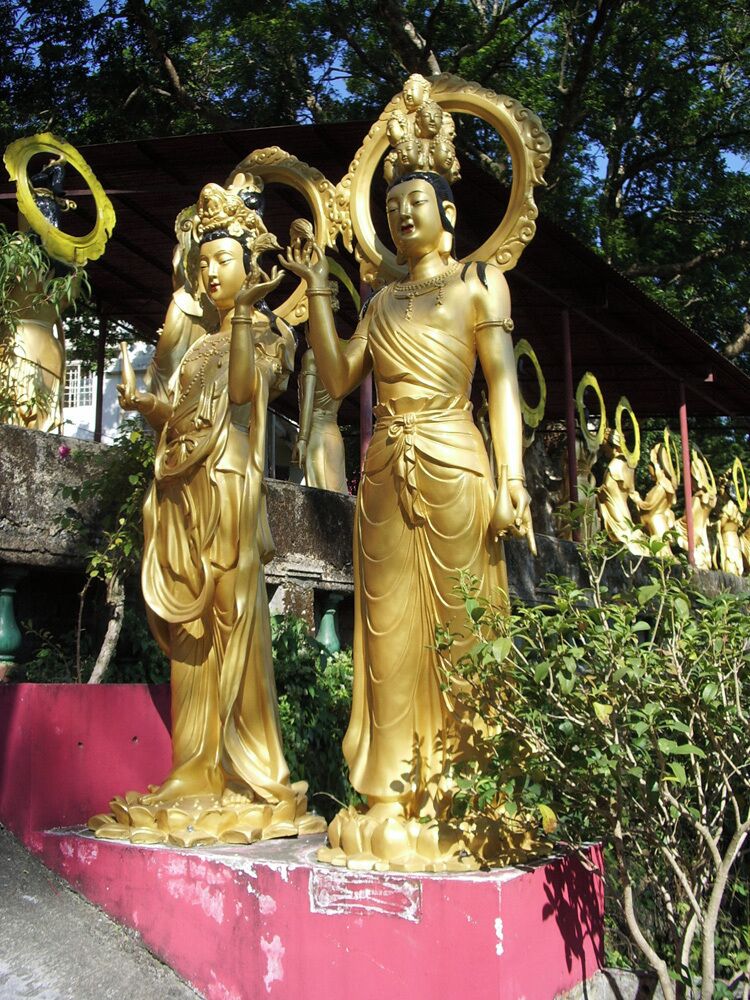 Golden statues of deities with ornate headdresses, set against a backdrop of trees and a pink structure.