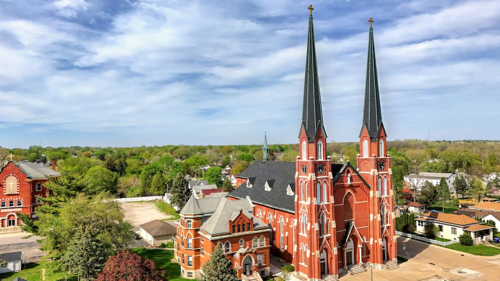 A red brick church with twin spires and a smaller adjacent building.