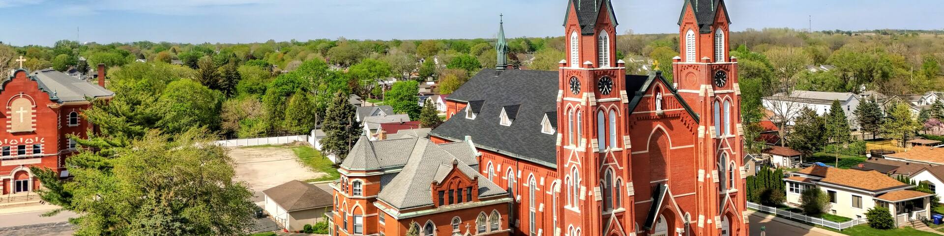 A red brick church with twin spires and a smaller adjacent building.