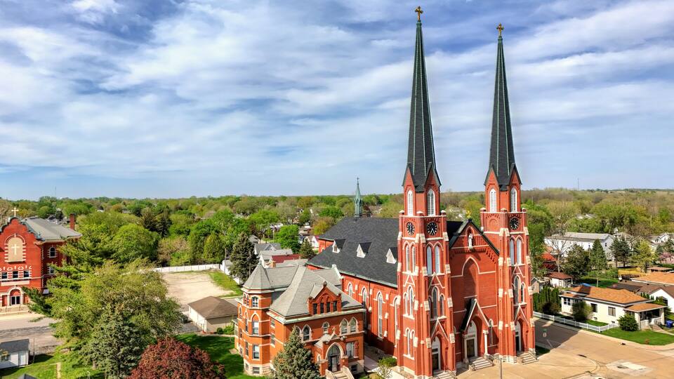 A red brick church with twin spires and a smaller adjacent building.