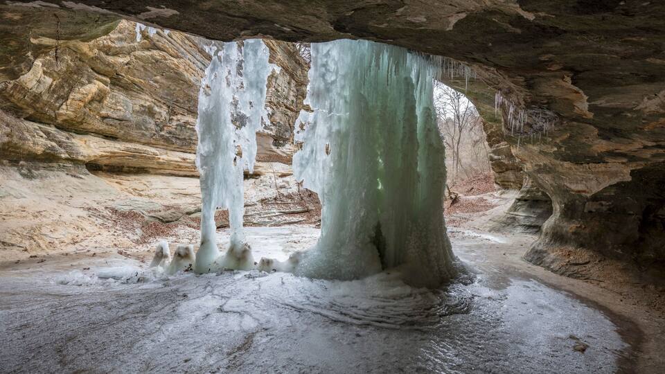 A cave with large ice formations and a sandy floor.