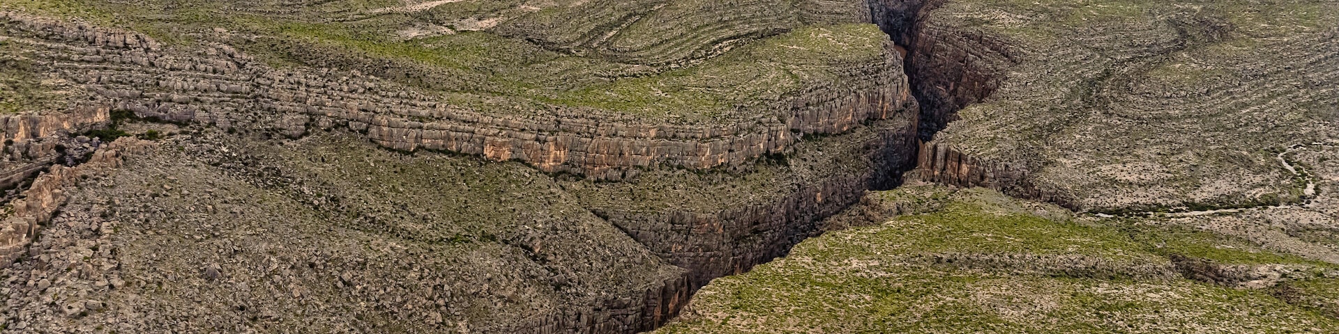Un cañón con formaciones rocosas estratificadas y un río que lo atraviesa.