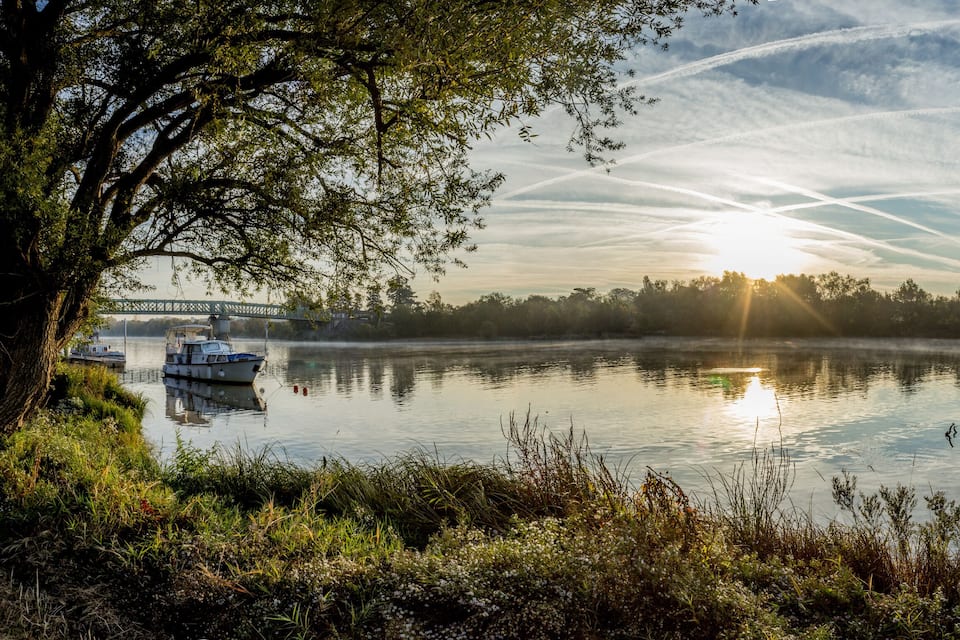 A calm lake with a boat, trees, and a bridge in the background.