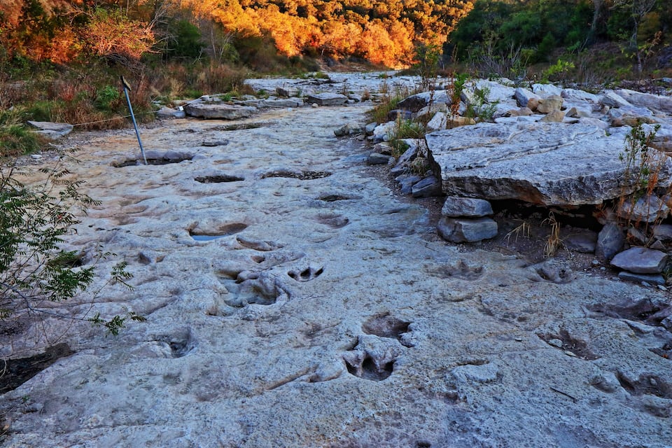 A rocky riverbed with footprints and a metal pole.