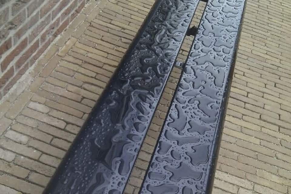 Een metalen bank met waterdruppels, geplaatst op een geplaveid voetpad.