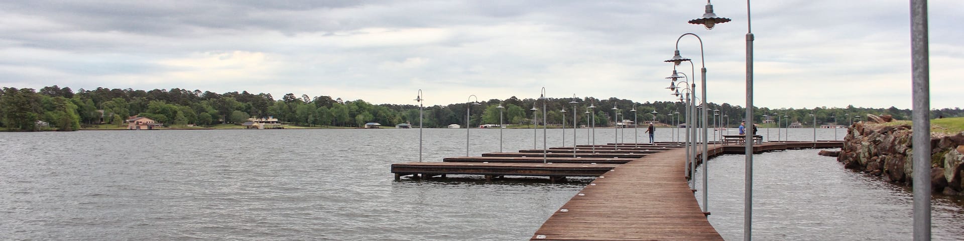 A wooden pier extending into a body of water, lined with street lamps.