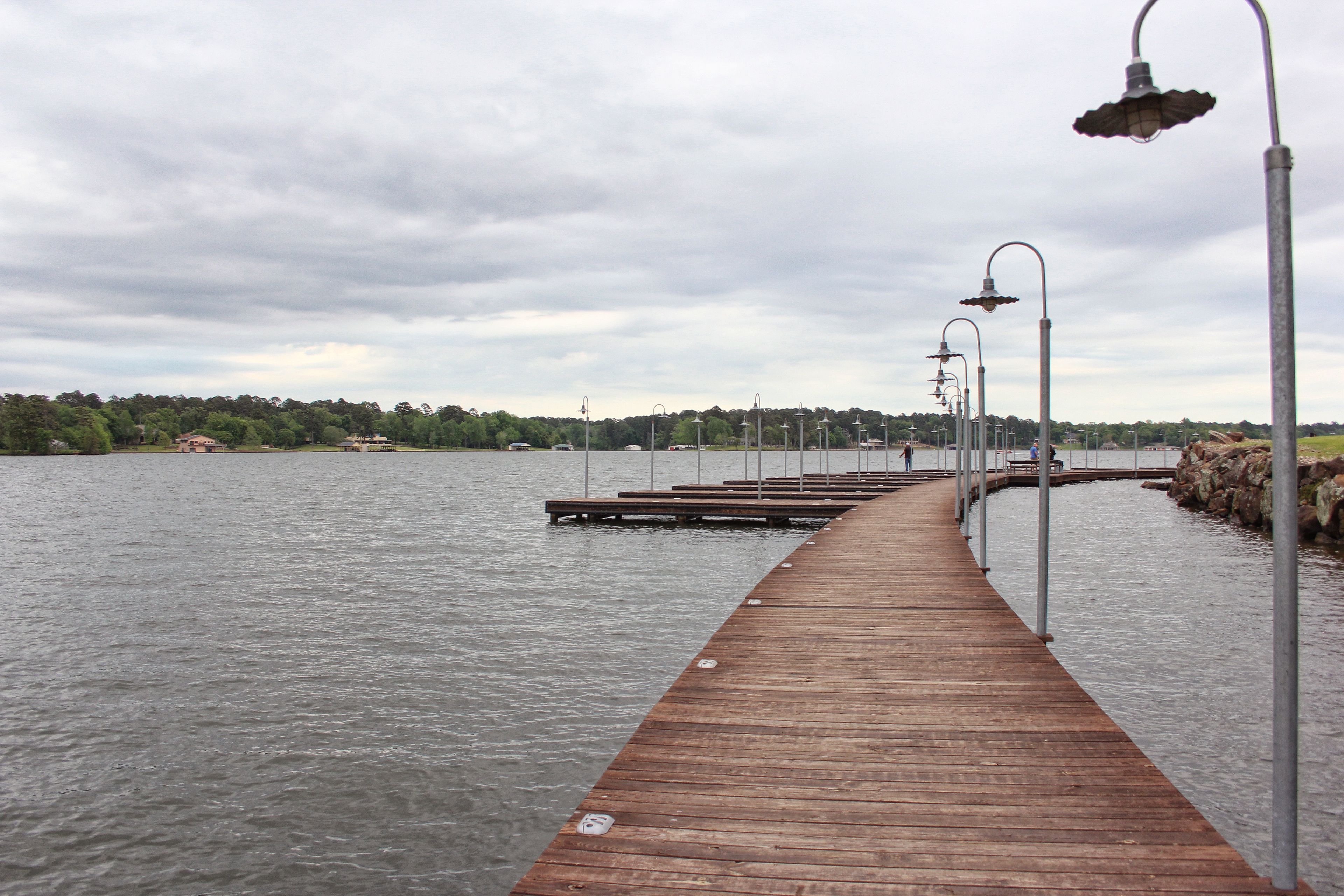 A wooden pier extending into a body of water, lined with street lamps.