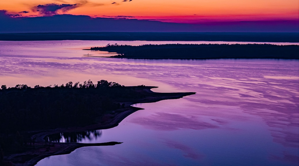Ein Sonnenuntergang über einem stillen See mit bewaldeter Uferlinie und entfernten Landformen.