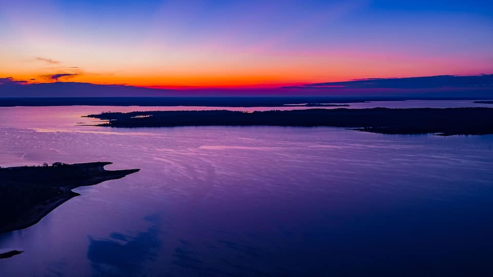 A sunset over a calm lake with a silhouette of a peninsula and distant land.