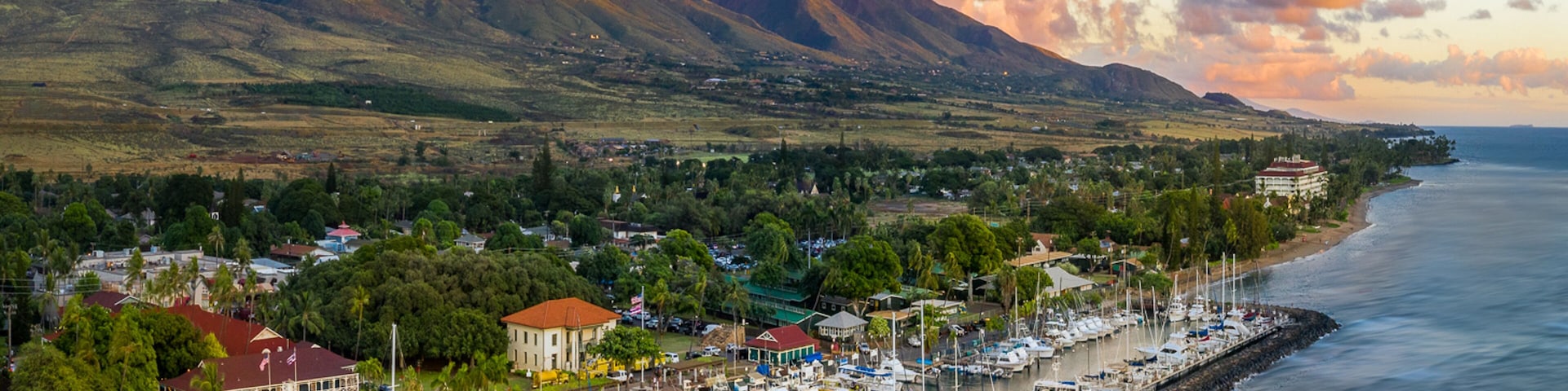 A coastal town with a marina, mountains in the background, and a clear sky.