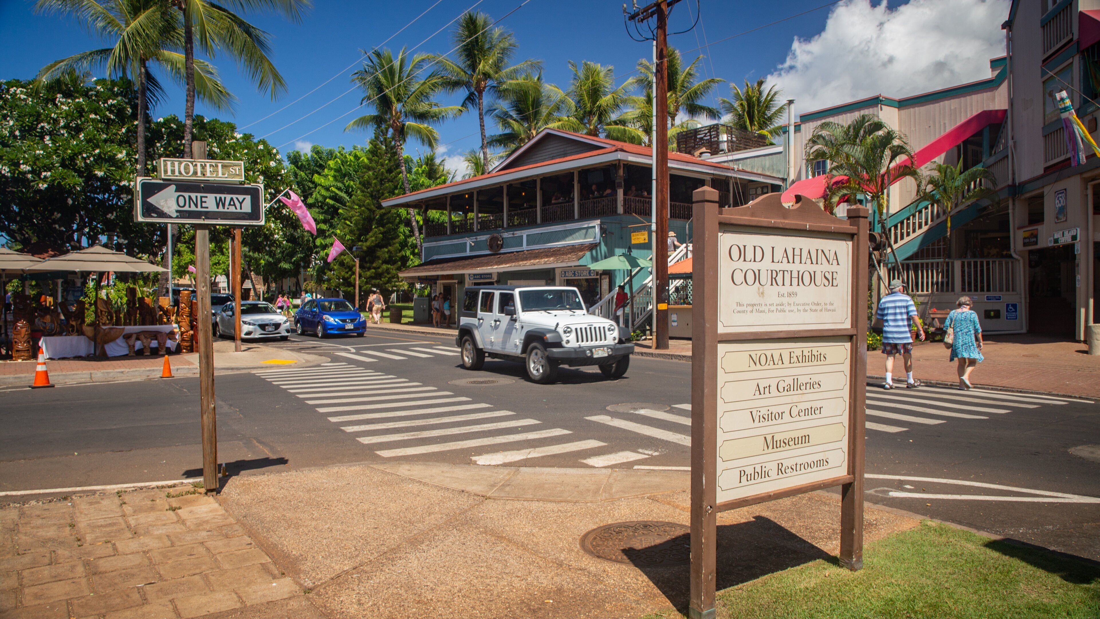 A street with a sign for Old Lahaina Courthouse, a blue car, and palm trees.
