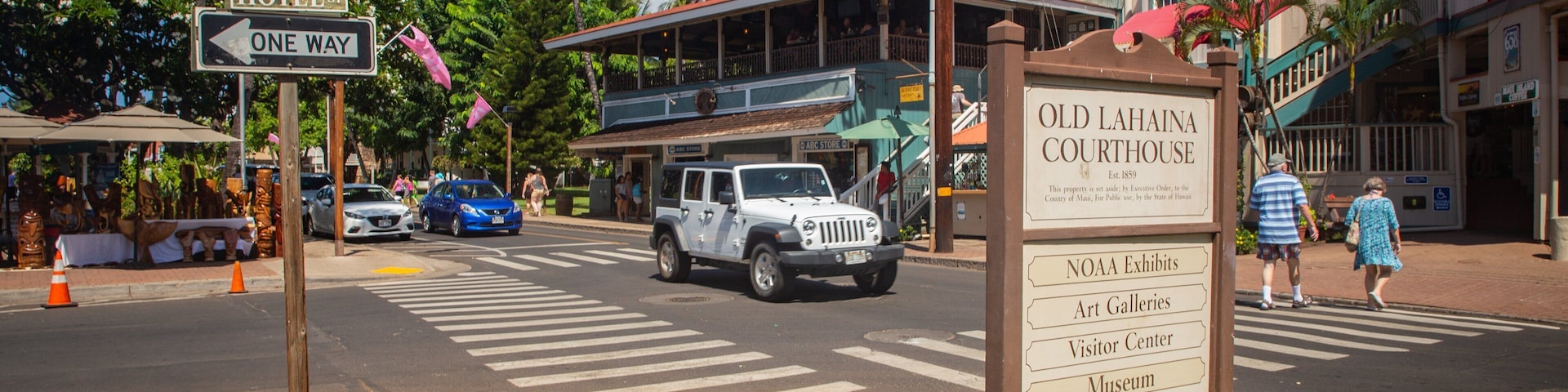 Una calle con un cartel que indica el Palacio de Justicia de Old Lahaina, un coche azul y palmeras.