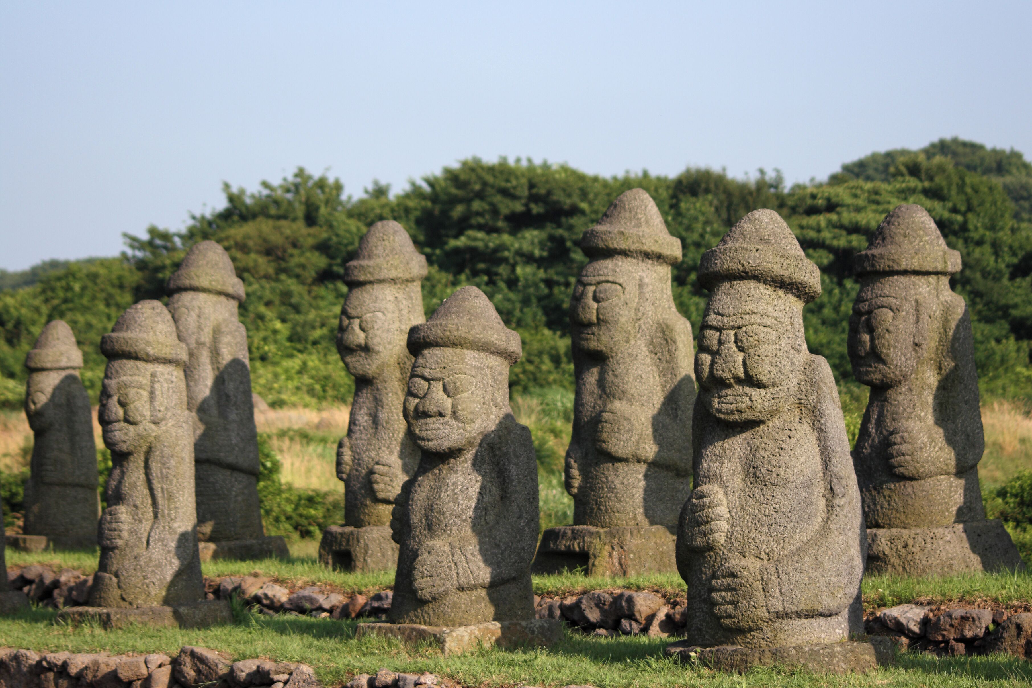 Una hilera de estatuas de piedra en un campo cubierto de hierba, con árboles al fondo.