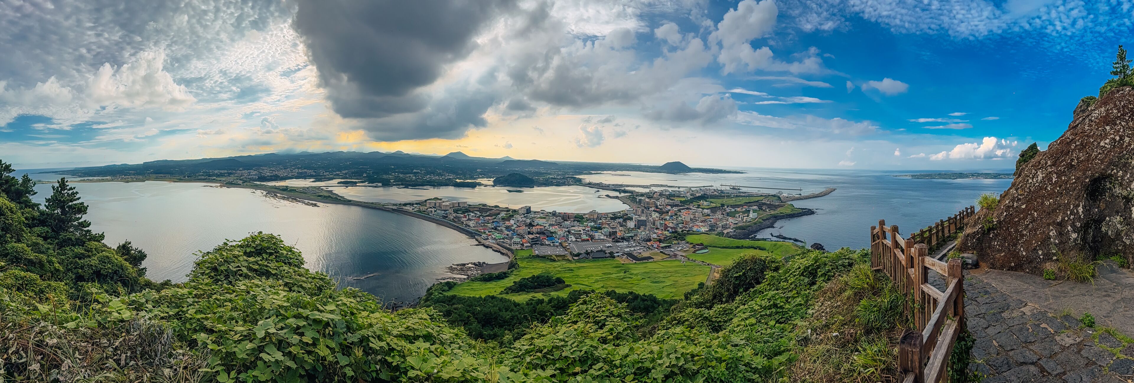 A coastal city with a large bay, surrounded by mountains and greenery.