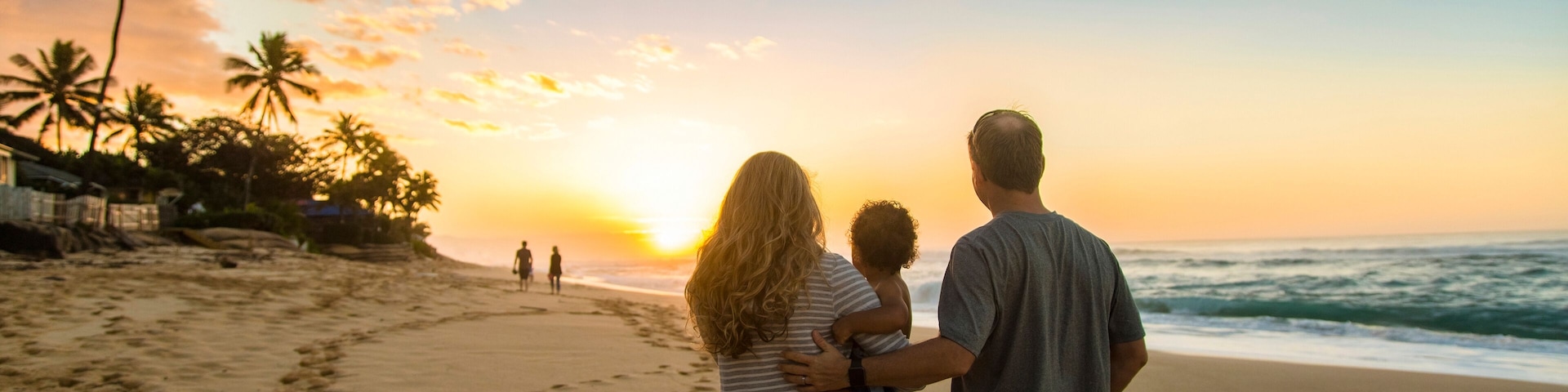 Pôr do sol em uma praia com pegadas, palmeiras e mar calmo.