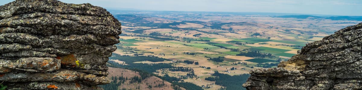 A rocky outcrop overlooking a valley with fields and distant hills.