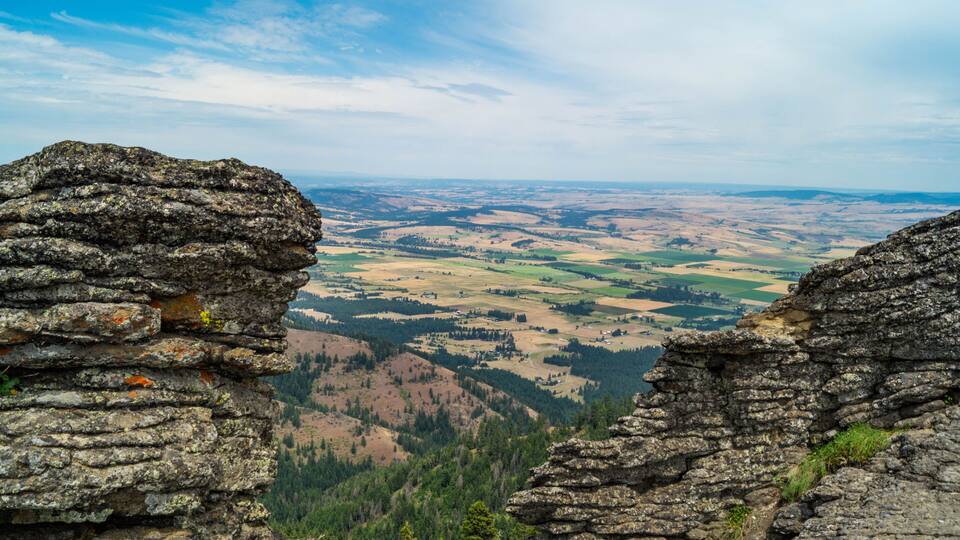A rocky outcrop overlooking a valley with fields and distant hills.