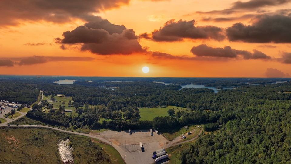 A sunset over a forested landscape with a river and a parking lot.