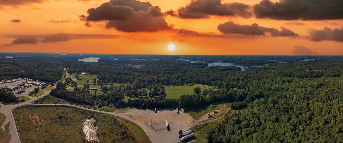 A sunset over a forested landscape with a river and a parking lot.