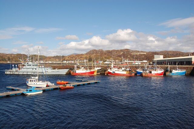 A harbor with several boats docked at piers, a large ship, and a mountainous landscape in the background.