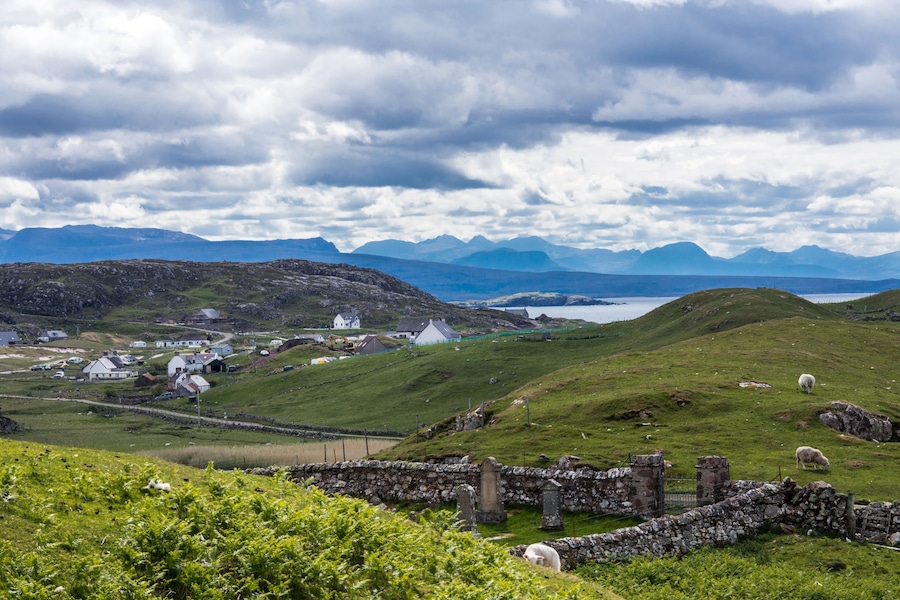 Assynt Peninsula, Scotland - June 7, 2012: The hamlet of Lochinver sits on the shore of Loch Inver an arm of the Atlantic Ocean. Blue-gray cloudscape and green pasture upfront. Horizon of mountains.