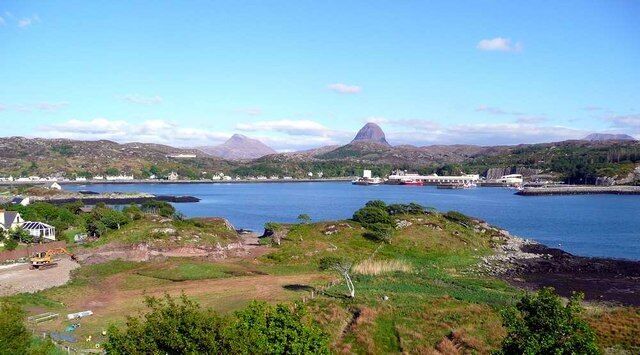 A coastal landscape with a large body of water, a prominent mountain, and industrial buildings.