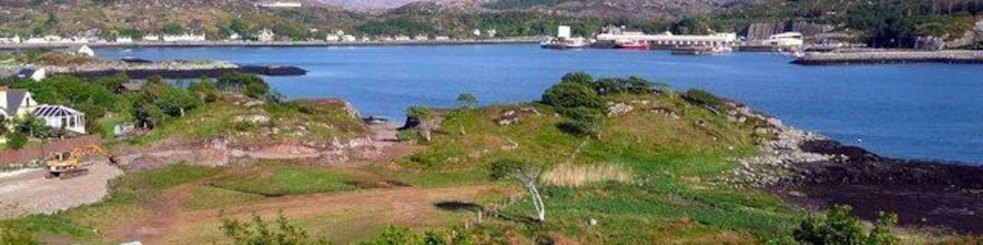 A coastal landscape with a large body of water, a prominent mountain, and industrial buildings.