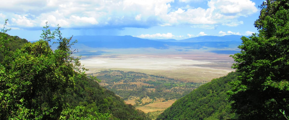 A valley with lush greenery and distant mountains under a partly cloudy sky.