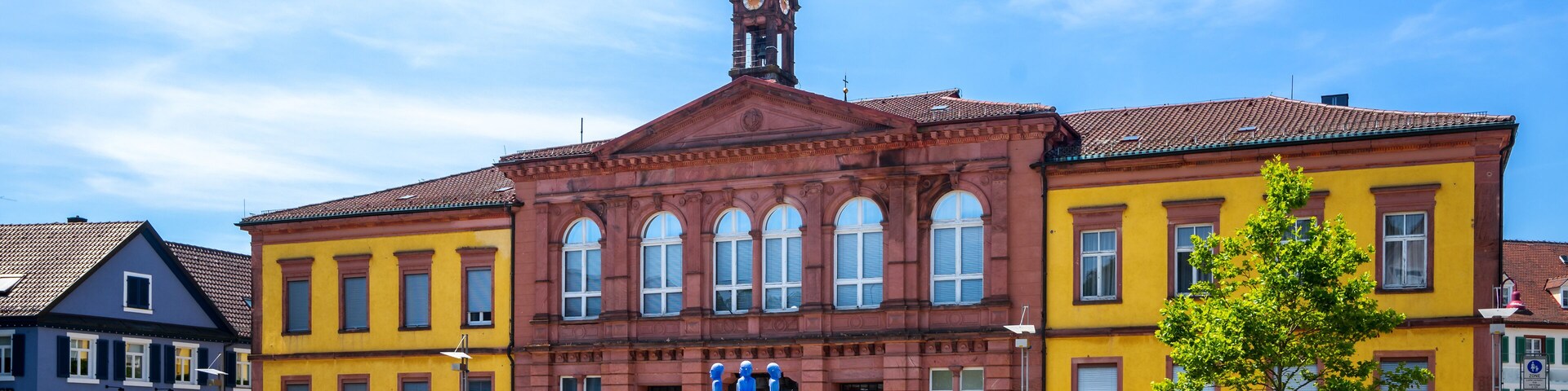 Um edifício histórico com uma torre do relógio, rodeado por edifícios coloridos e um céu azul límpido.