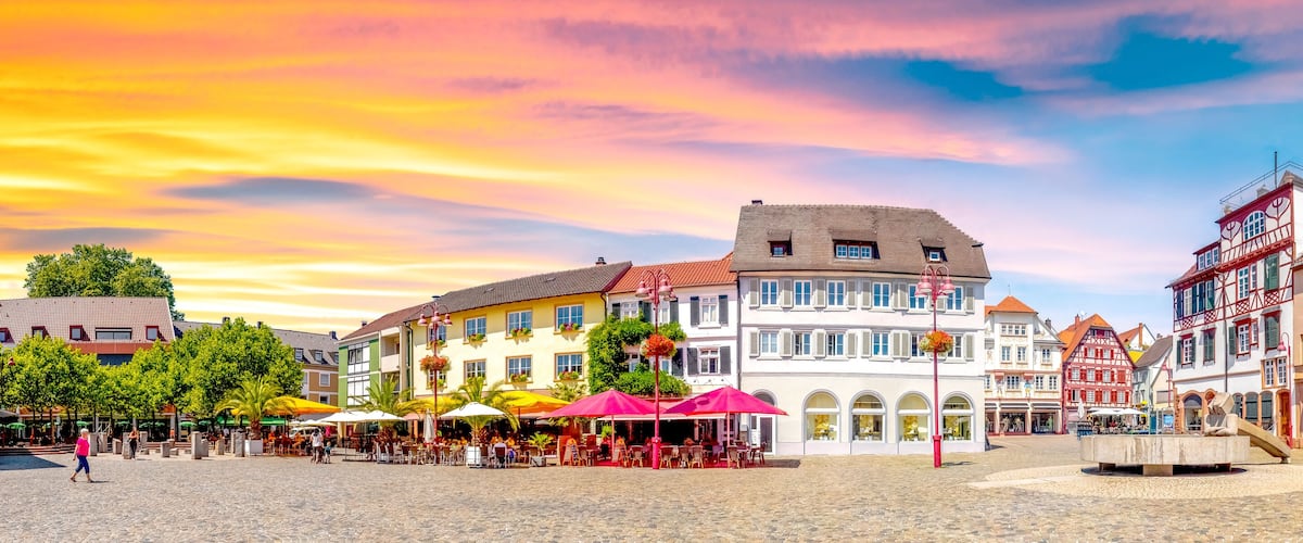 A cobblestone square with historic buildings, outdoor cafes, and a fountain.