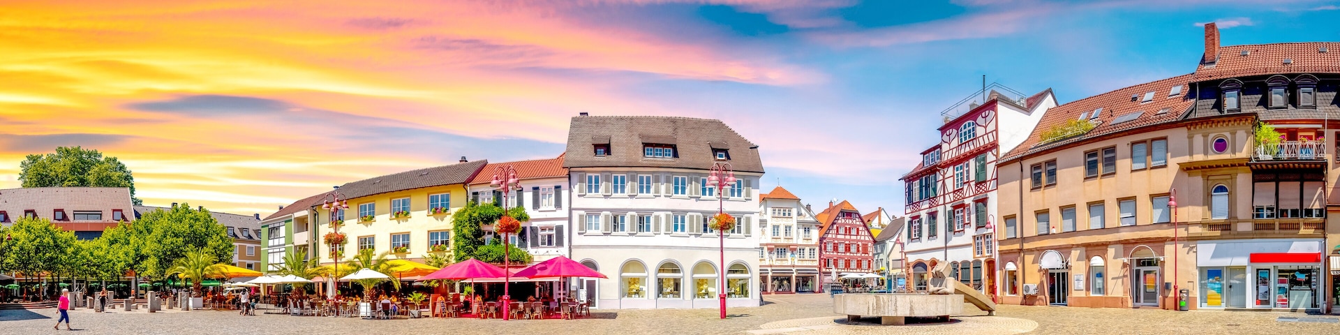 A cobblestone square with historic buildings, outdoor cafes, and a fountain.