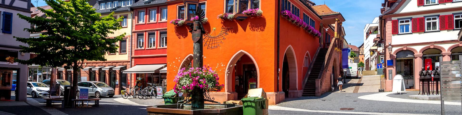 A vibrant orange building with a green spire, surrounded by traditional European architecture.