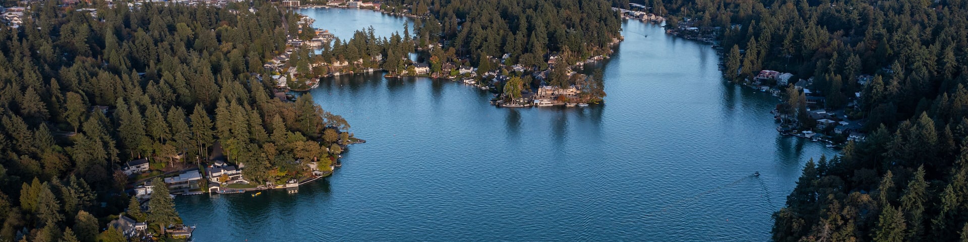 Aerial drone picture of Lake Oswego, Oregon and Mount Hood in backgrond, showing calm blue water surrounded by dense forest and residential houses, real estate, on a clear sunny evening at sunset.