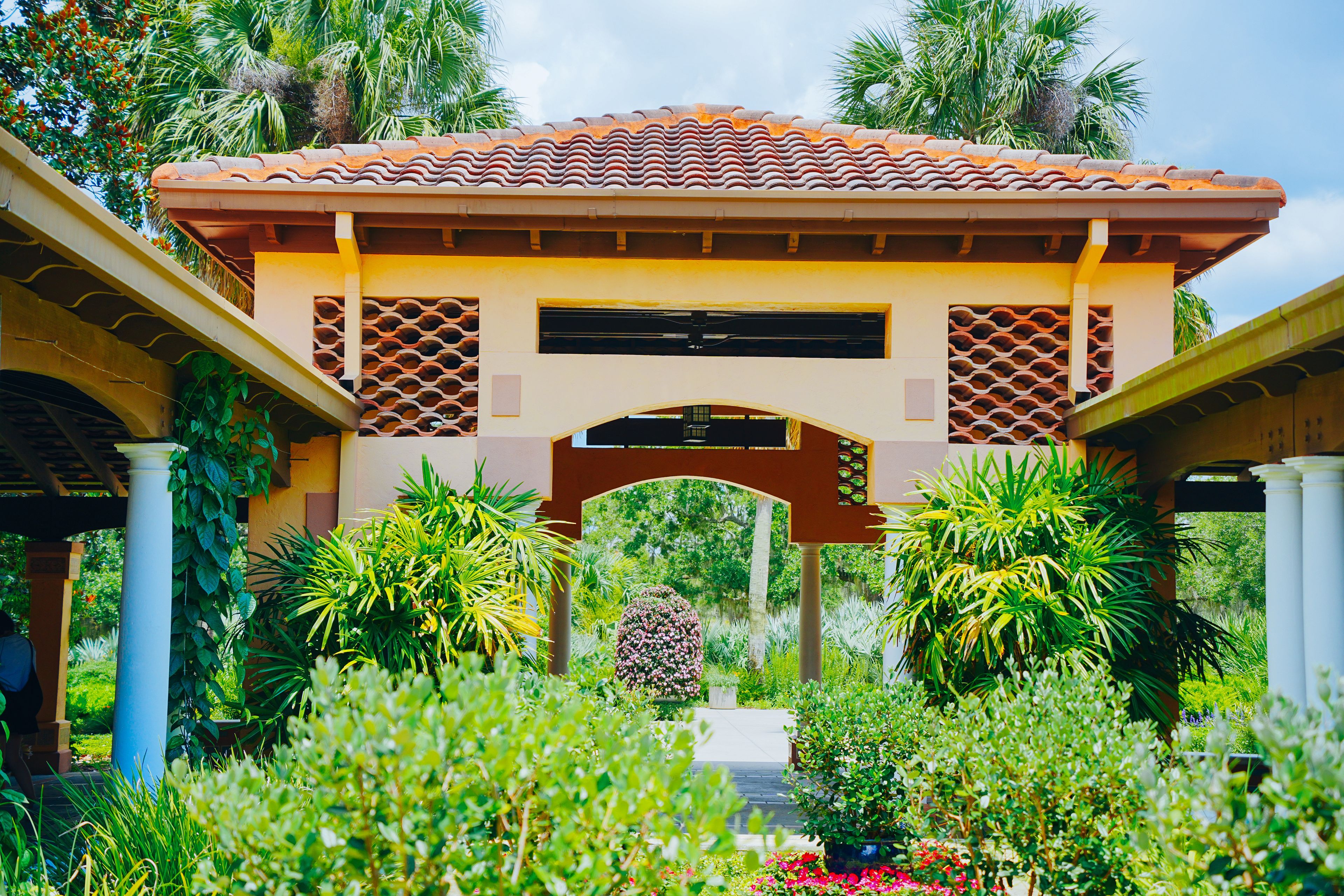 A traditional pavilion with terracotta roof tiles, surrounded by lush greenery and palm trees.