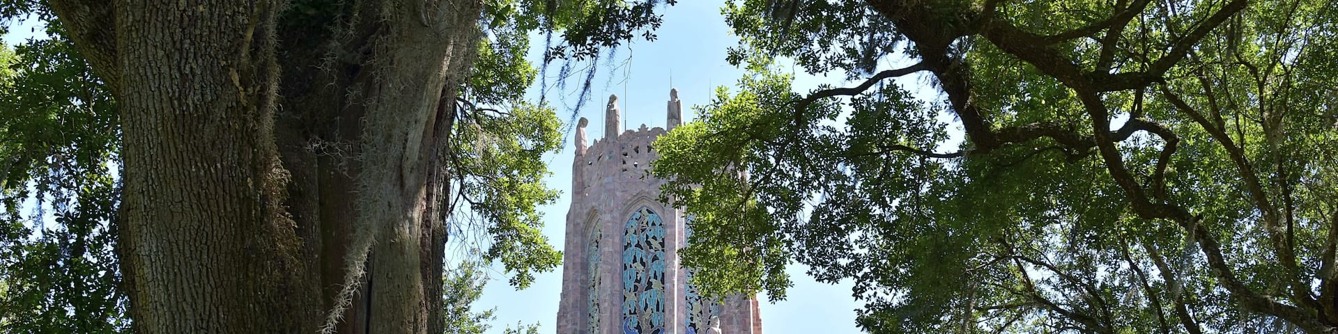 A tall tower with intricate stained glass windows, surrounded by lush green trees.