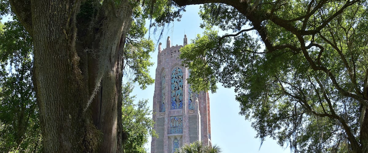 A tall tower with intricate stained glass windows, surrounded by lush green trees.