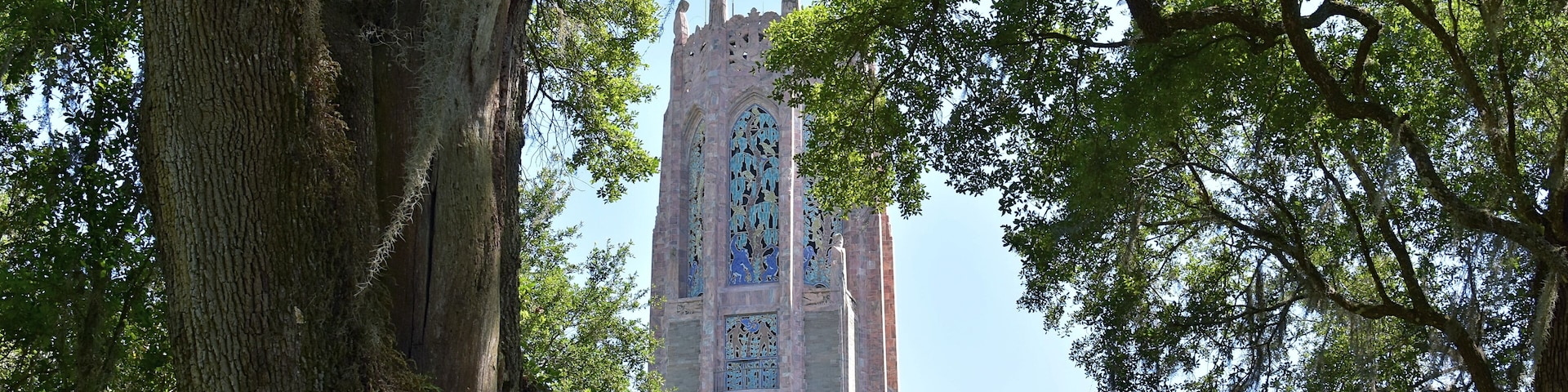 A tall tower with intricate stained glass windows, surrounded by lush green trees.