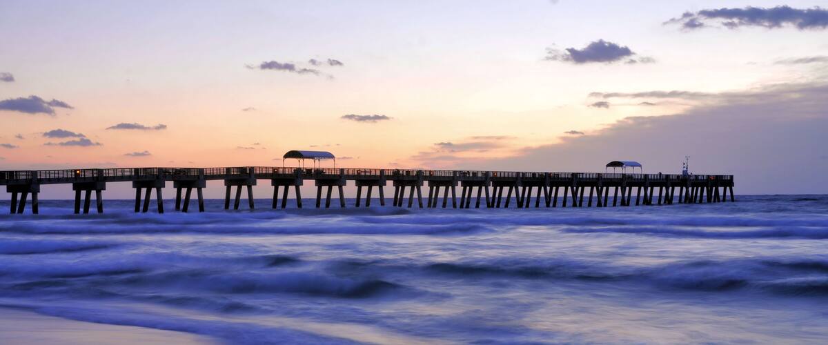 A pier extending into the ocean with a sunset in the background.
