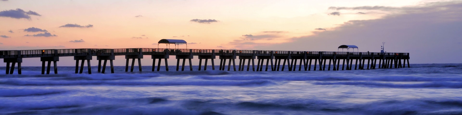 A pier extending into the ocean with a sunset in the background.