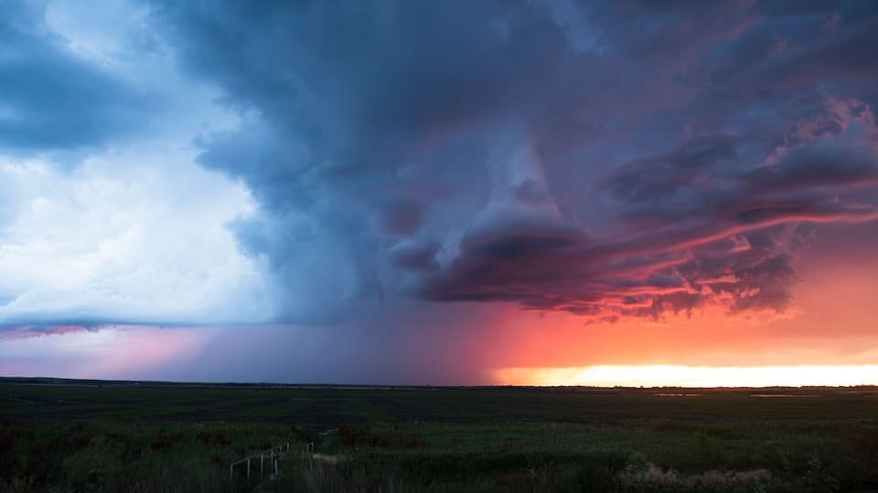 A vast open field under a dramatic sky with a sunset.