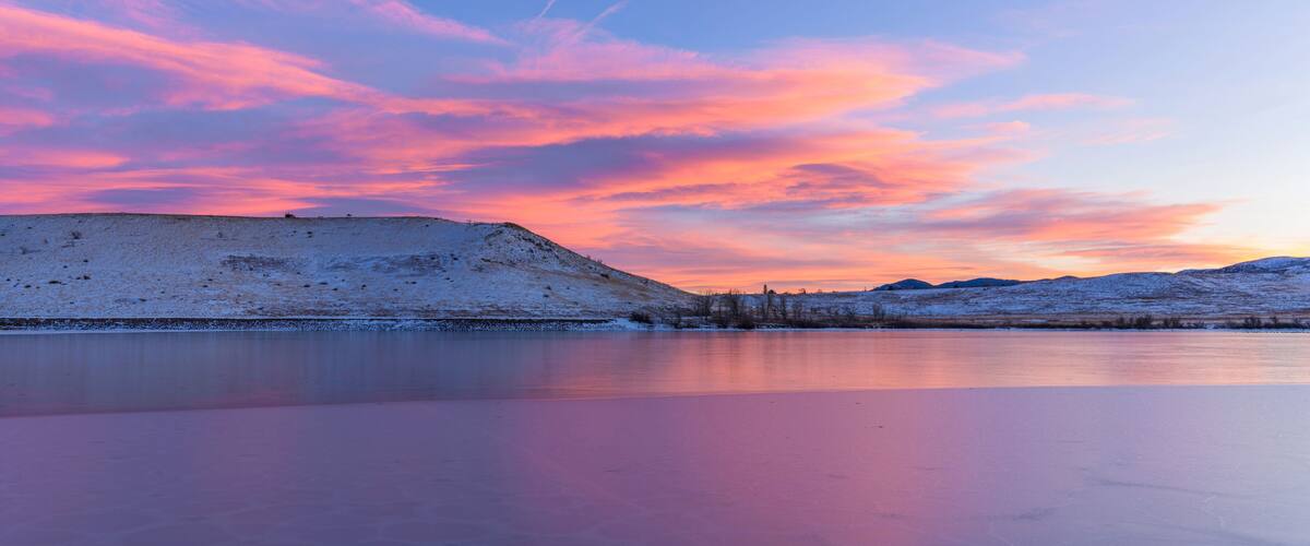 A frozen lake with a snow-covered hill and a sunset sky.