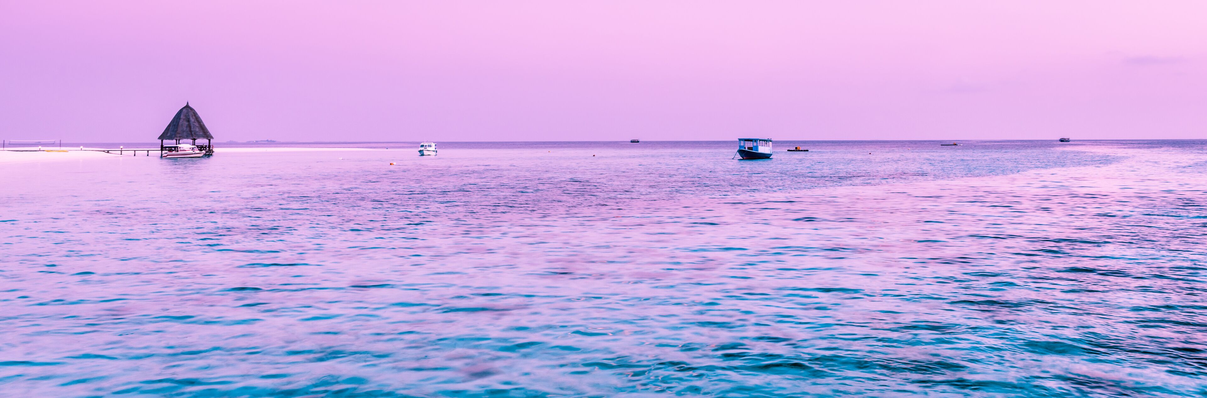 A calm sea with a thatched-roof hut and several boats.